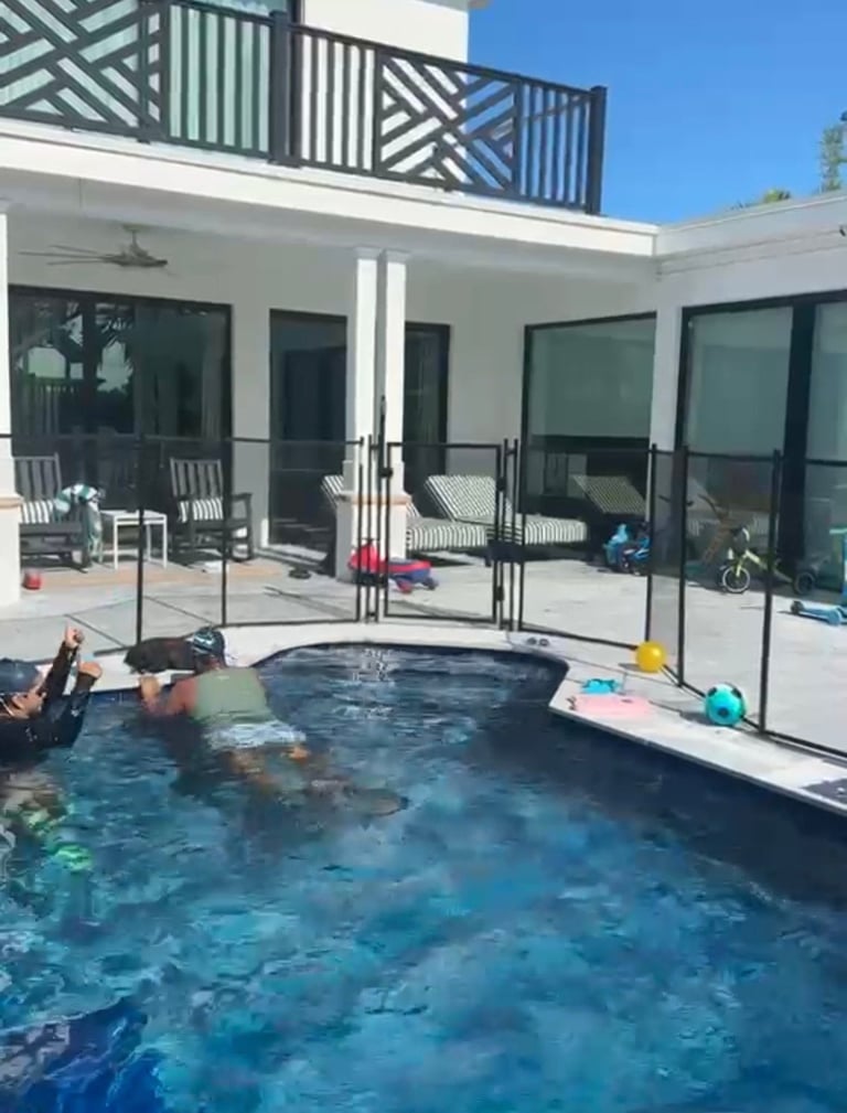 Modern backyard with swimming pool, hot tub, white house with black-framed glass doors, and second-floor balcony with geometric railings
