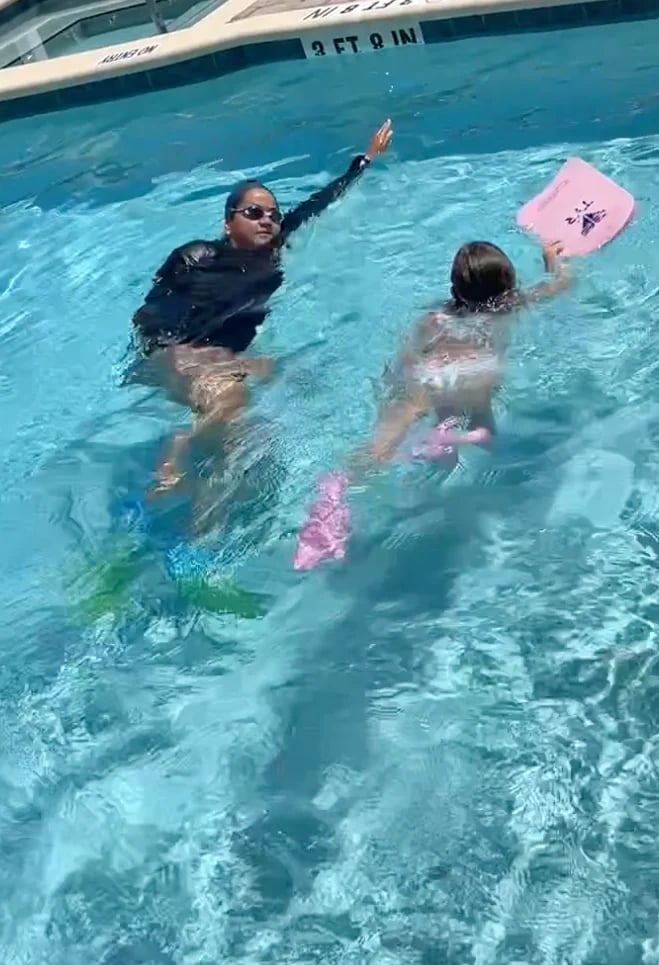 Adult swimming instructor teaching two children in a bright blue pool with pink kickboards