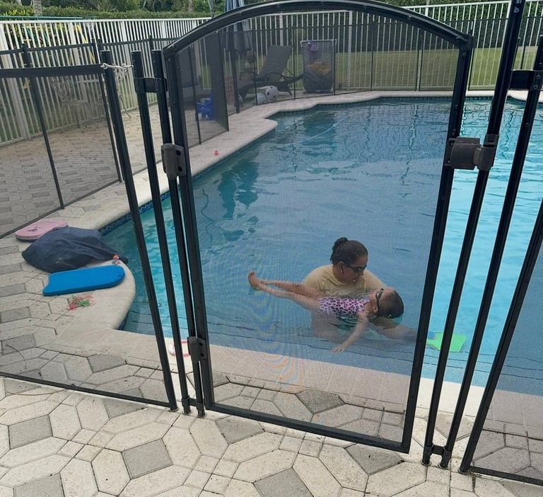 Child swimming in pool viewed through black safety fence gate