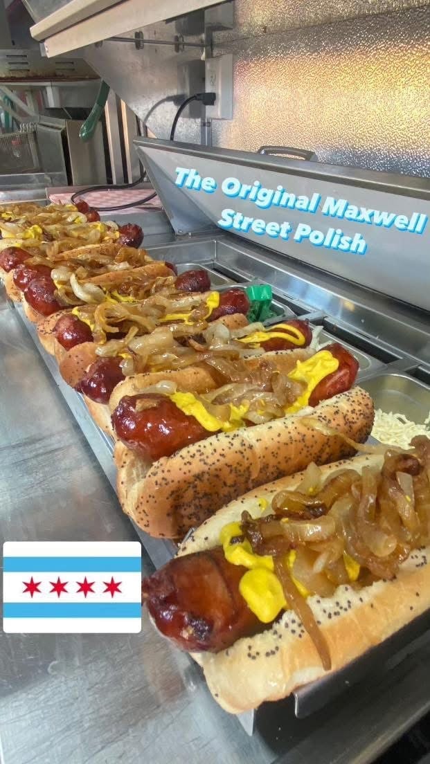 Row of Chicago-style hot dogs with toppings and mustard displayed in a food truck service window