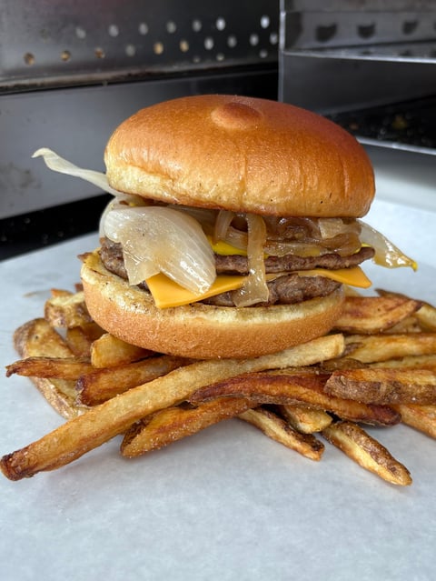 Gourmet cheeseburger with caramelized onions on a toasted bun, served with crispy french fries on a white plate