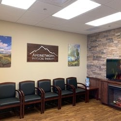 Waiting room with Apexworks Medical Group logo sign, five black chairs, wood flooring, brick accent wall, and framed landscape photos