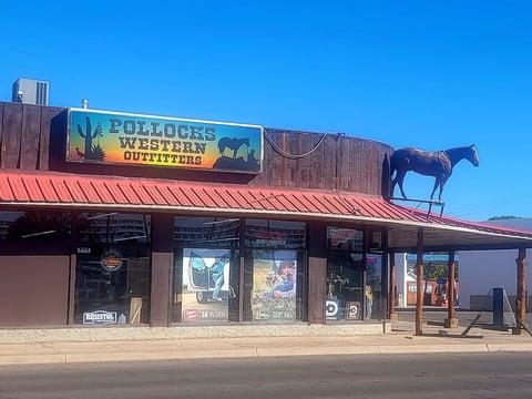 Pollocks Western Outfitters storefront with a red metal roof and silhouette of a horse on top against a clear blue sky