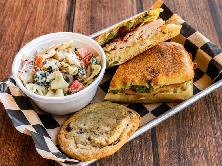 Deli platter with sandwich, skewers, garlic bread, and creamy salad on checkered paper and wooden surface
