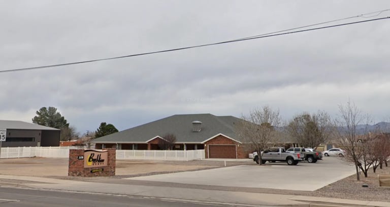BeeHive Homes of the Gila Valley — single-story brick assisted living facility with brown shingled roof, white porch railing, and brick sign with BeeHive Homes logo in front under cloudy sky