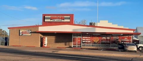 A red and tan vintage diner building with a mid-century modern architectural style, featuring large windows and signage, photographed from the street.