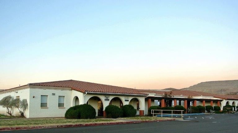 Single-story Mediterranean-style building with white walls, arched entrance, and clay tile roof next to parking area at dusk