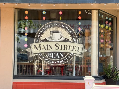 Main Street Beanery storefront with large coffee cup logo on window and hanging colorful lanterns
