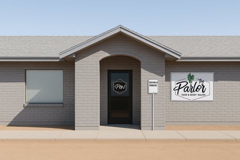 Modern barber shop storefront with brick exterior, black door, windows, and signage in desert setting