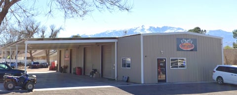 Metal commercial building with open bays, vehicles parked outside, bare trees and snow-capped mountains in background