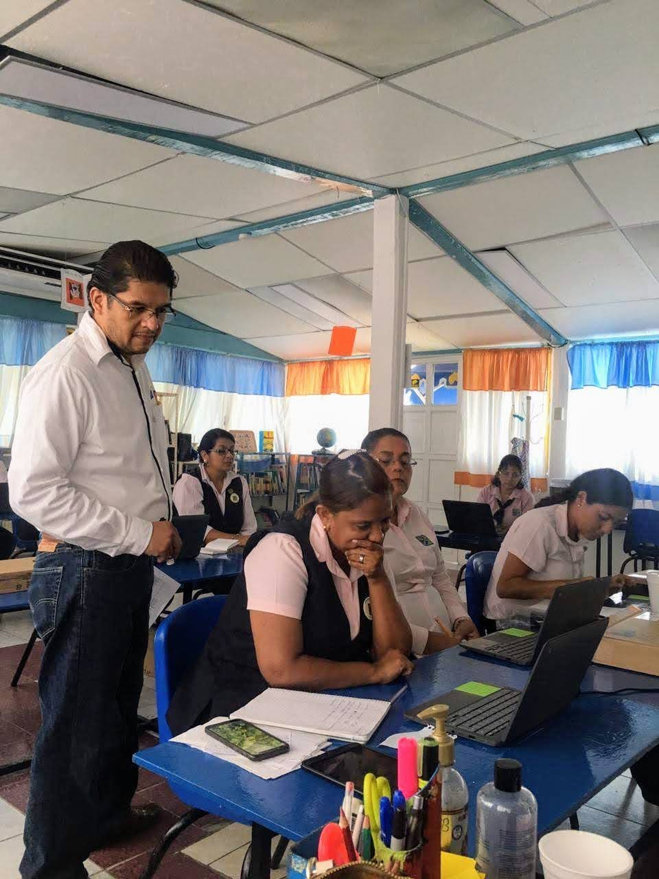 Raúl Reyes asesorando personalmente a una emprendedora con su laptop — mentoría práctica en un salón de clases