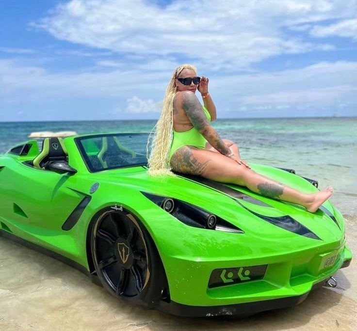 Woman in sunglasses posing on bright green sports car in shallow beach water