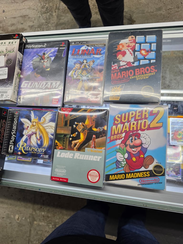 Retro video game collection displayed in glass case showing Mario and Nintendo titles on PlayStation 2, NES, and Game Boy