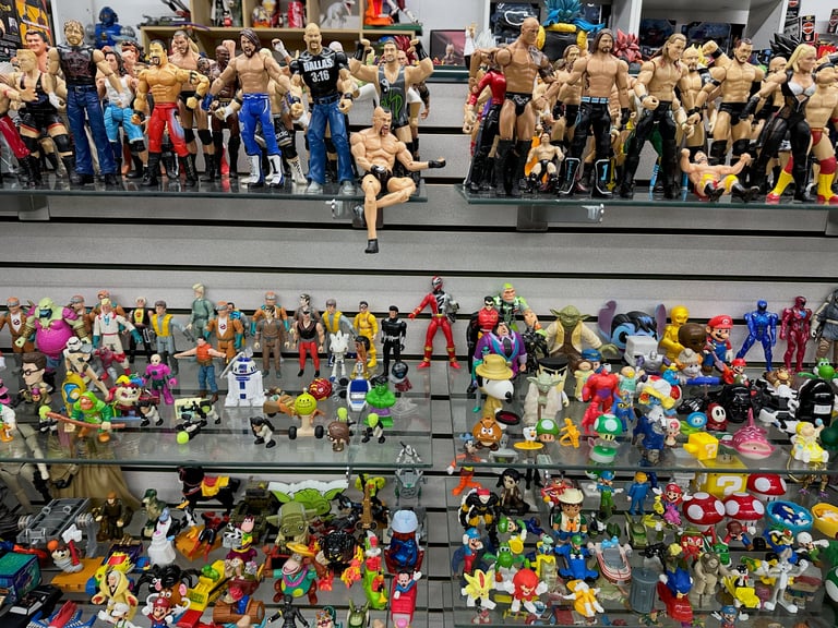 Large collection of action figures and toys displayed on tiered shelves at what appears to be a convention or toy show