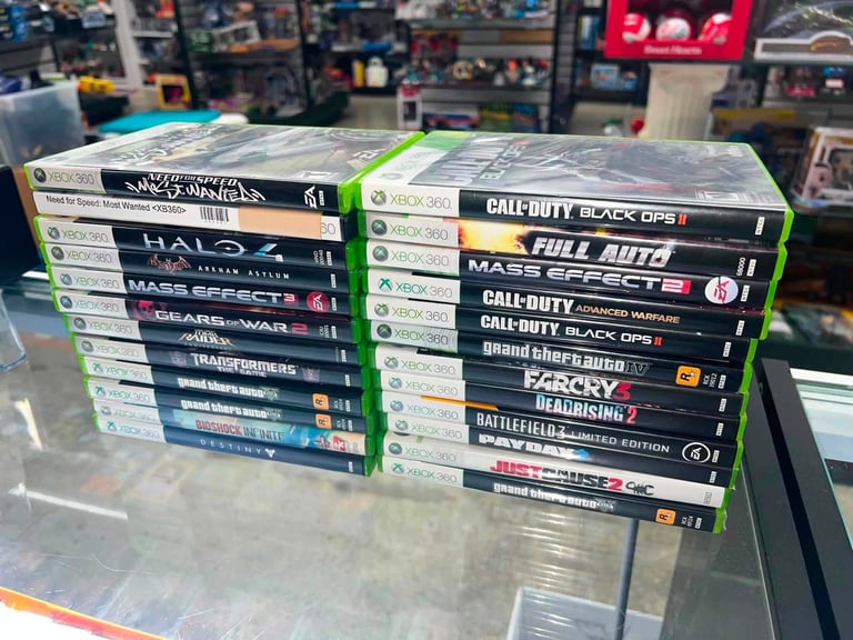 Collection of Xbox 360 video game cases stacked in two piles on a glass counter in a game store