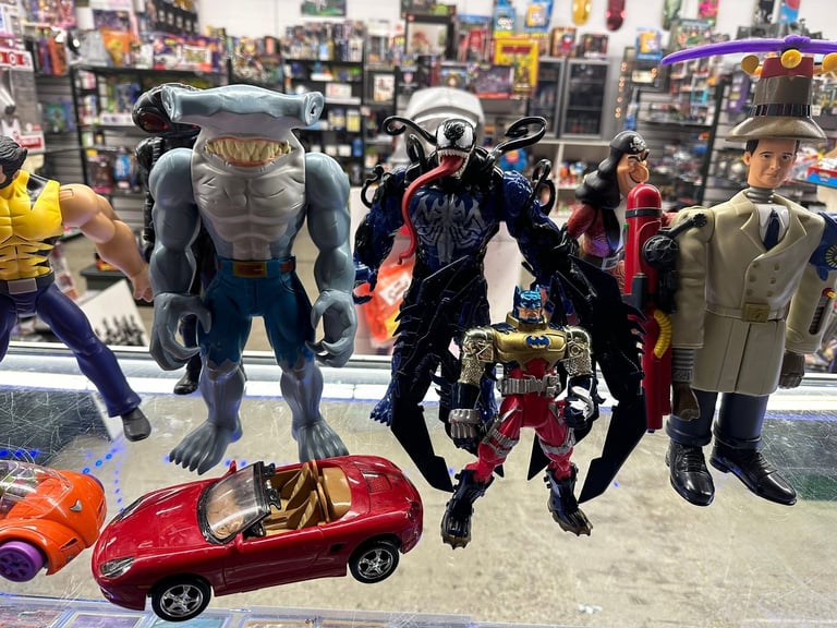 Collection of action figures and toys displayed in a comic shop, featuring superhero and character figurines of varying sizes.