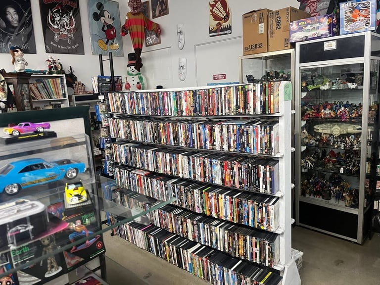 A collection room with a large white shelving unit displaying hundreds of movies and DVDs, toy cars, collectible figures in a display case, and wall decorations