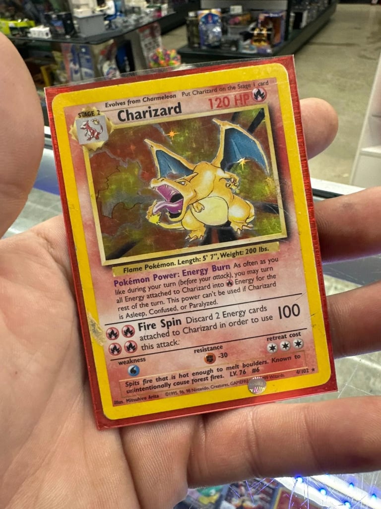 Hand holding a vintage Charizard Pokémon trading card with yellow border, showing the flame Pokémon at 120 HP