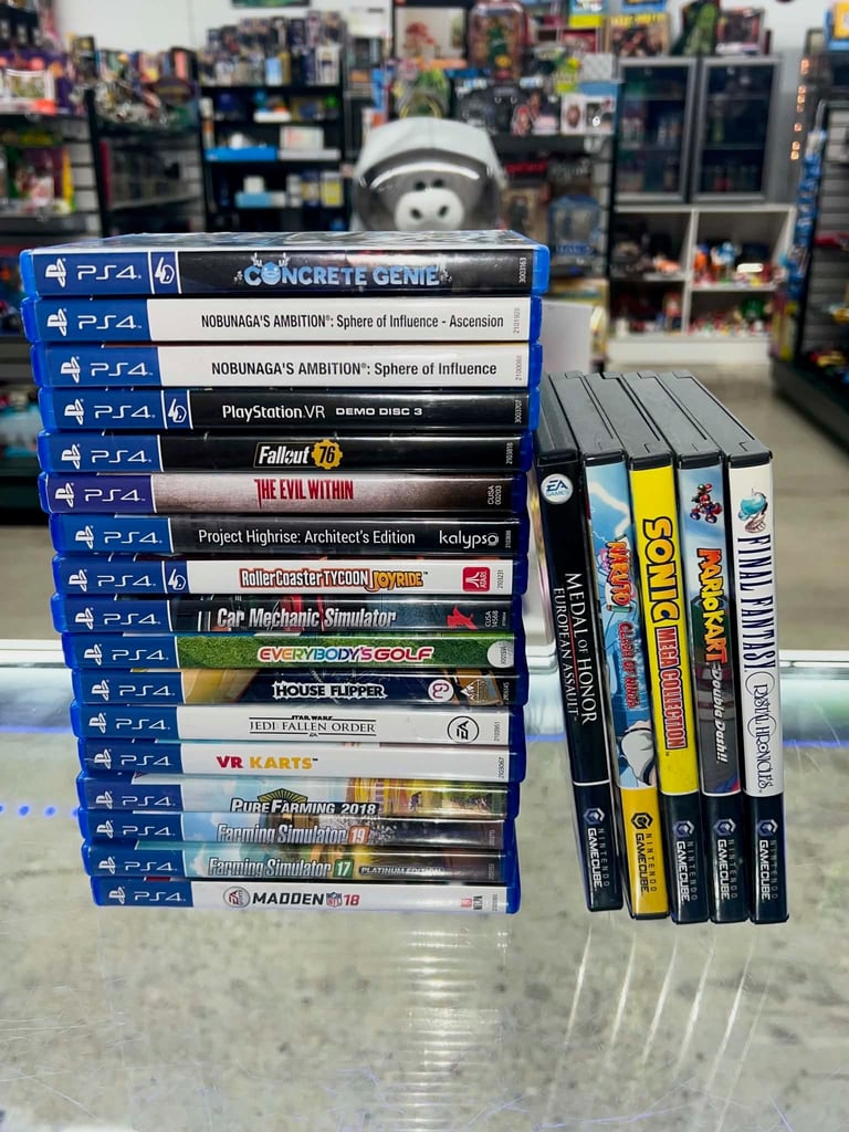 Stacked collection of PS4 video games and other gaming titles displayed on a retail counter with collectibles visible in the background