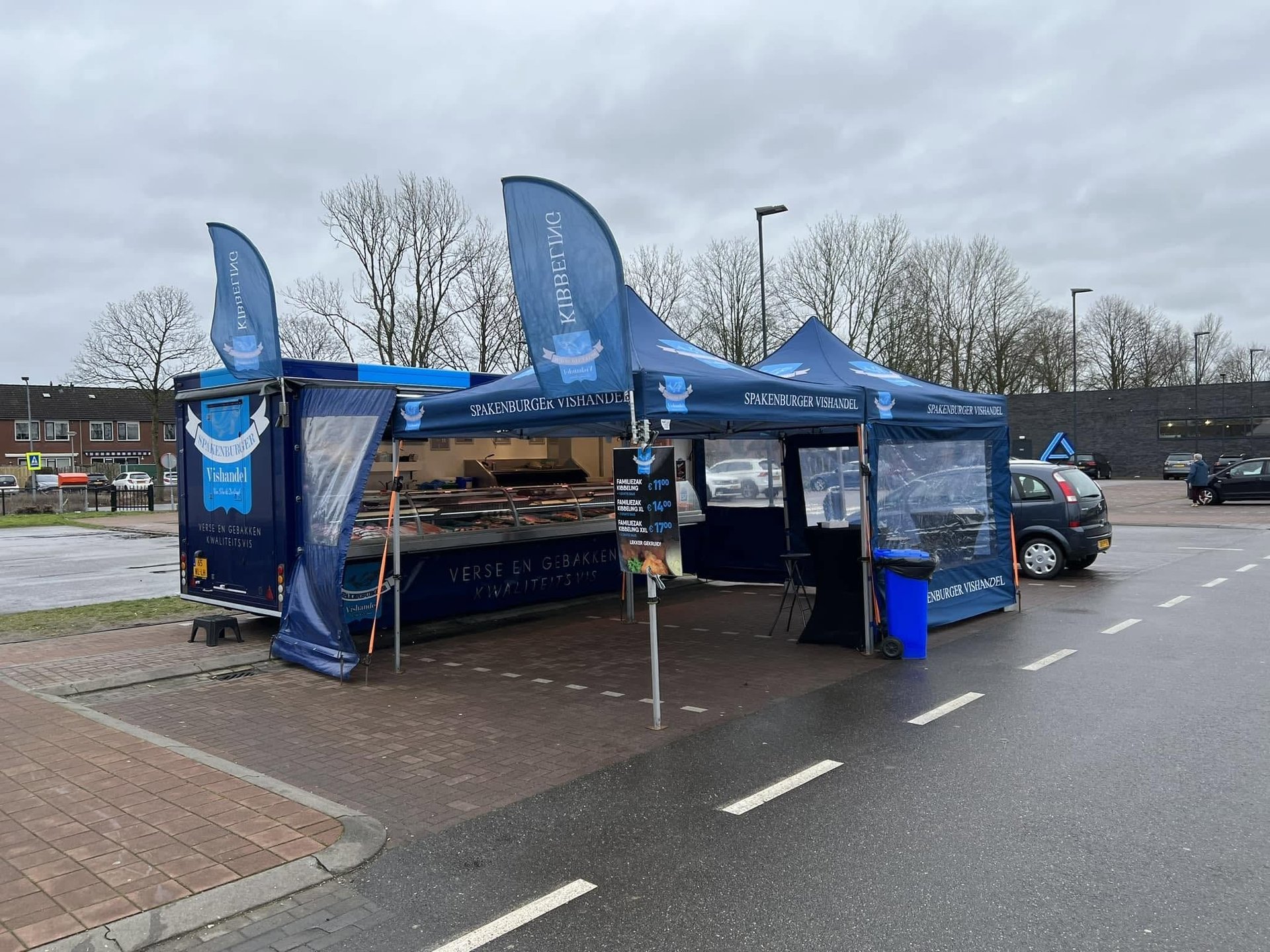 Blauwe marktkraam van Spakenburger Vishandel met vlaggen op een parkeerterrein