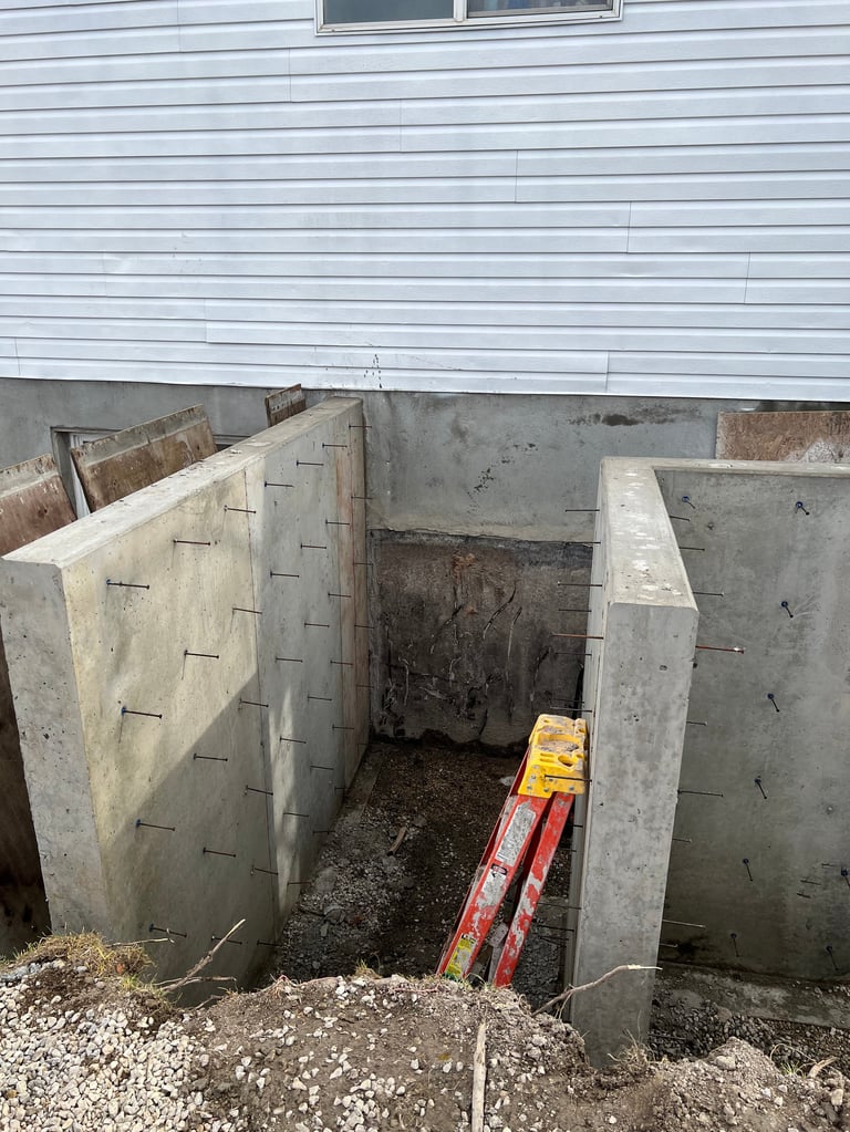 Concrete basement window well with metal ladder installed below light blue house siding