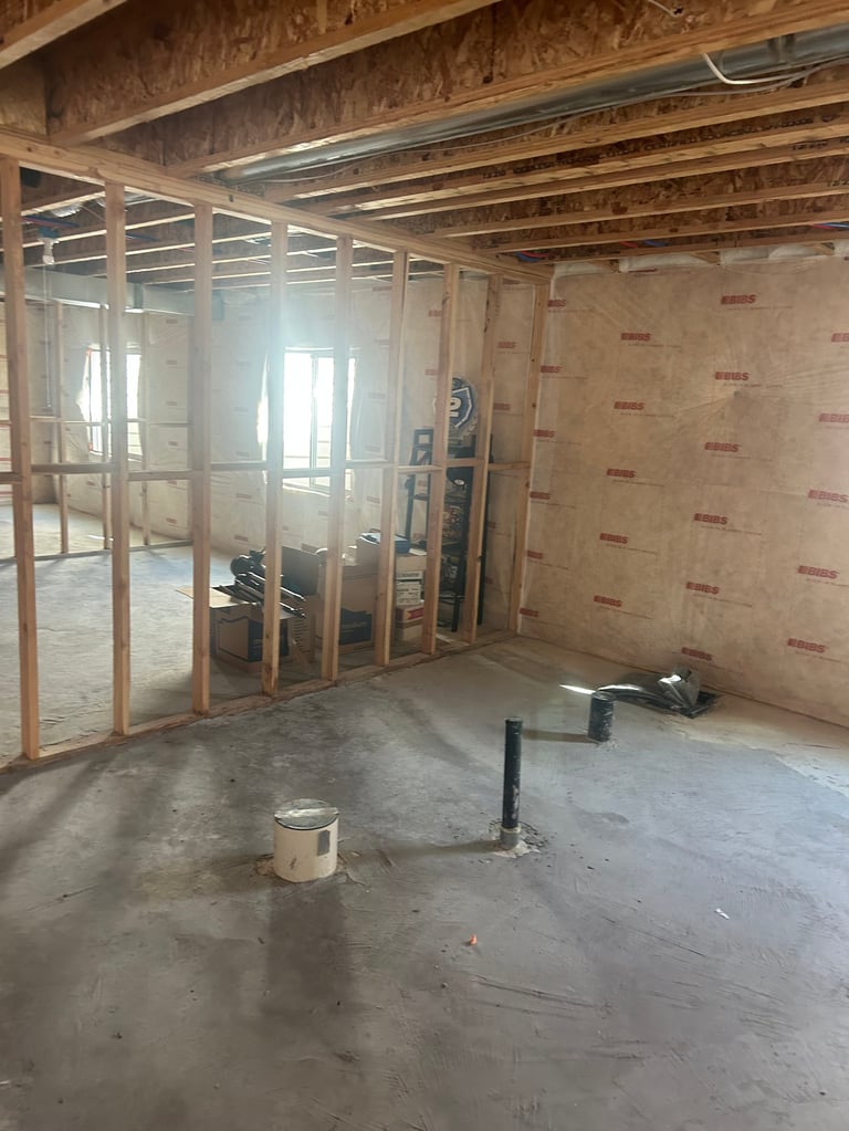 Interior of a construction room with exposed framing, drywall, concrete floor, and glass partition wall during renovation