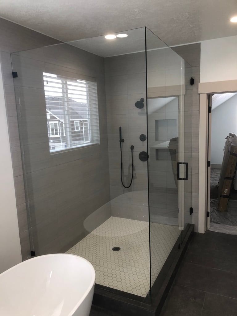 Modern bathroom with glass-enclosed walk-in shower, gray wall tile, white hexagon floor tile, and a bright window