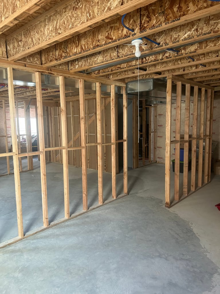 Interior construction framing with wooden wall studs, exposed ceiling joists, and concrete floor during renovation