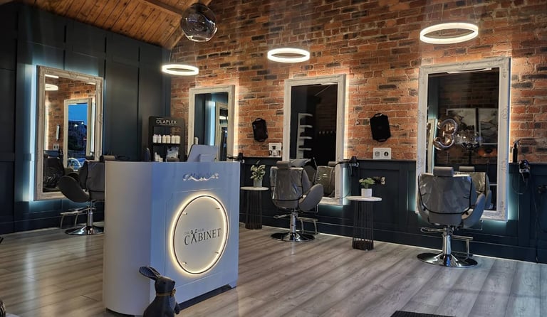 Modern hair salon interior with wooden floors, brick walls, illuminated mirrors, and styling stations with black chairs