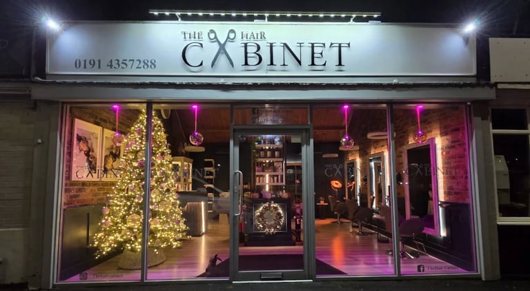 The Q Hair Cabinet storefront at night with illuminated pink neon lighting and gold decorative elements on the windows