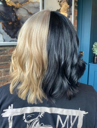 Back view of split-dyed hair styled in waves: platinum blonde on left side, jet black on right side