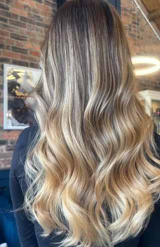 Back view of long wavy hair with balayage highlights transitioning from dark roots to blonde ends