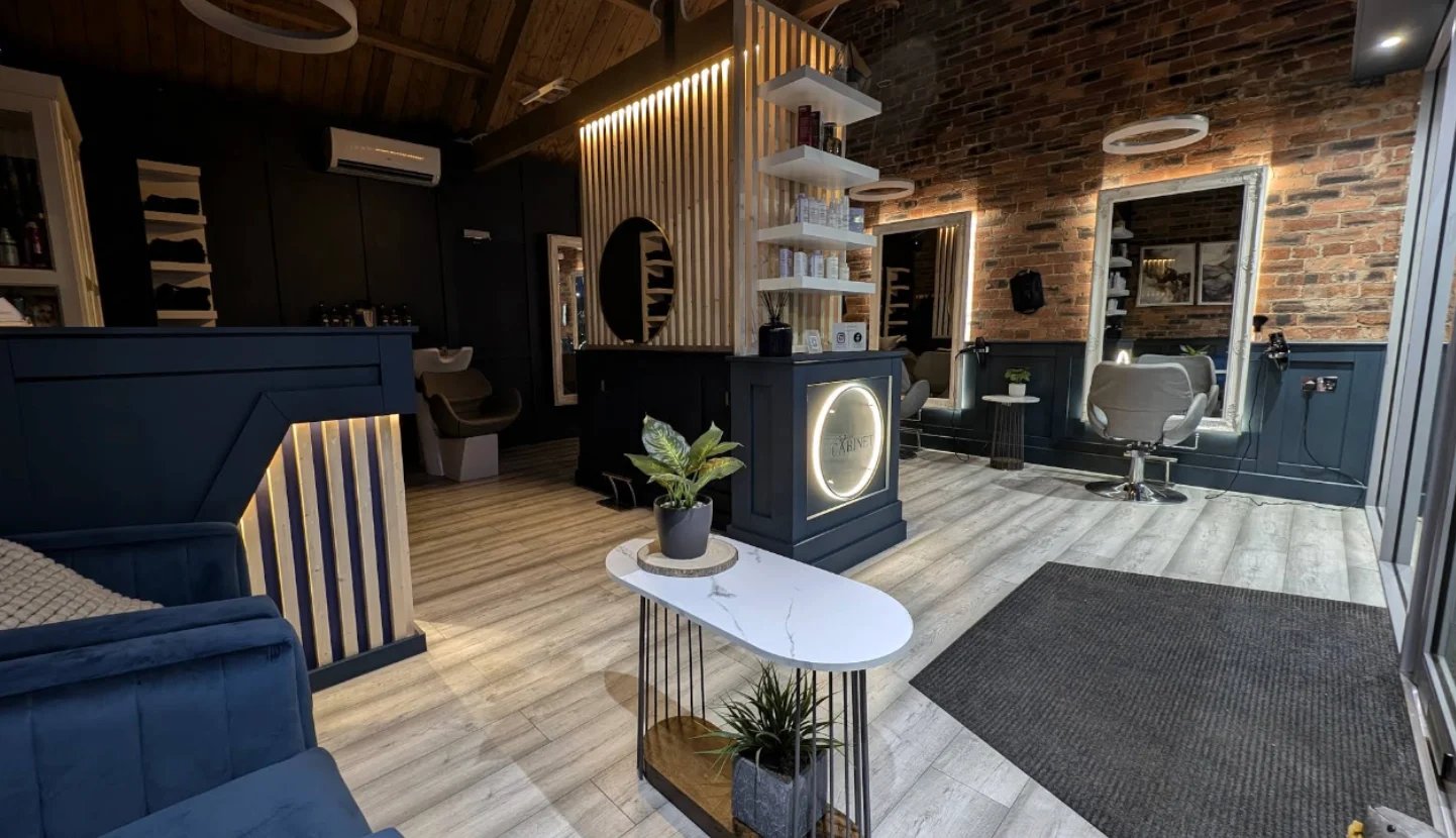 Modern hair salon interior with navy blue furniture, wooden floors, brick walls, mirrors, and contemporary lighting fixtures