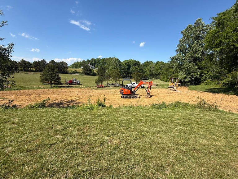 Red tractor in a rural field with freshly tilled soil, surrounded by green grass and trees under a clear blue sky