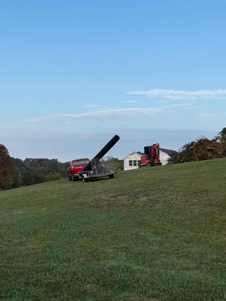 Red wood chipper truck on a green hillside with a white house and trees in the background under a blue sky