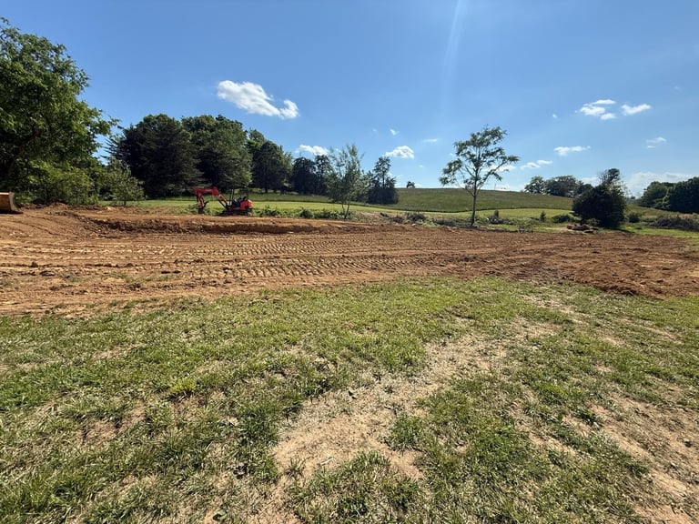 Agricultural field with newly tilled brown soil and green pasture beyond under blue sky