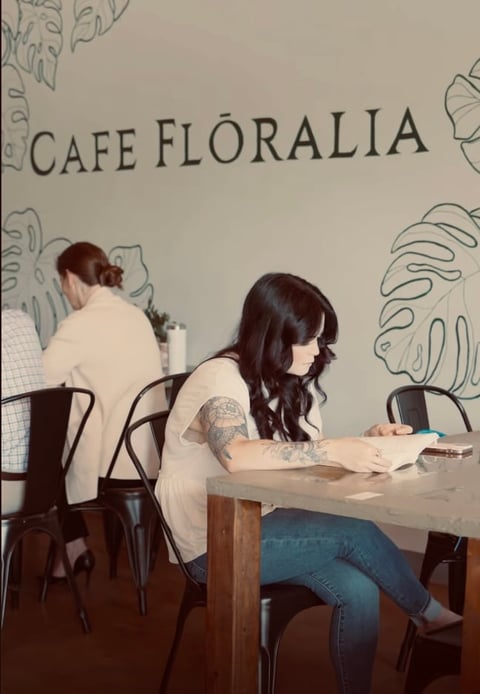 Two people seated at a table in Cafe Floralia with botanical wall drawings visible behind them