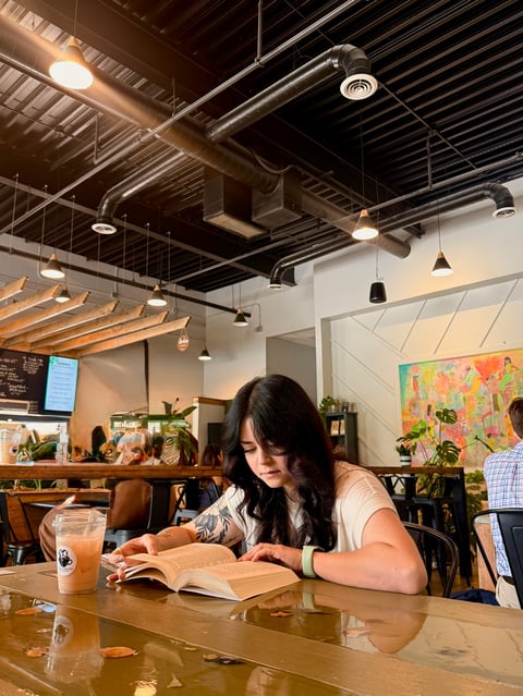 Woman reading a book at a wooden table in a modern cafe