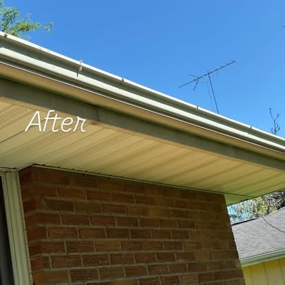 After: Renovated roof overhang with new green trim and gutters showing brick wall below and clear blue sky above
