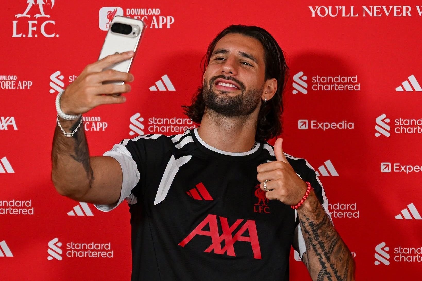 Man in black AXA shirt taking a selfie in front of red Liverpool FC branded backdrop with sponsor logos