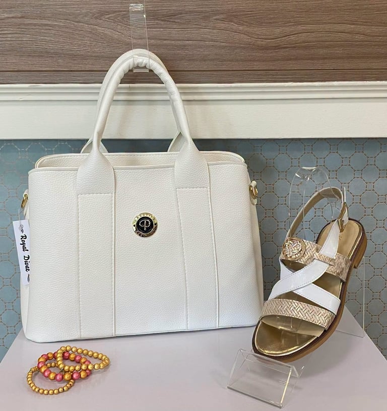 White quilted handbag with gold circle logo, gold and white strappy sandals, and beaded bracelets displayed on a light surface