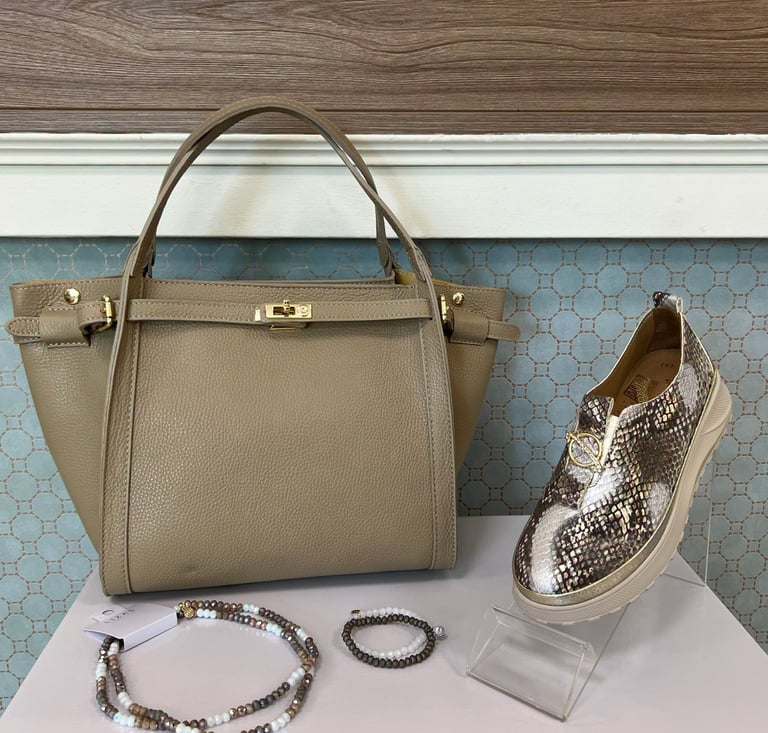 Beige leather handbag with handles, snakeskin slip-on sneaker, and beaded bracelets displayed on white surface