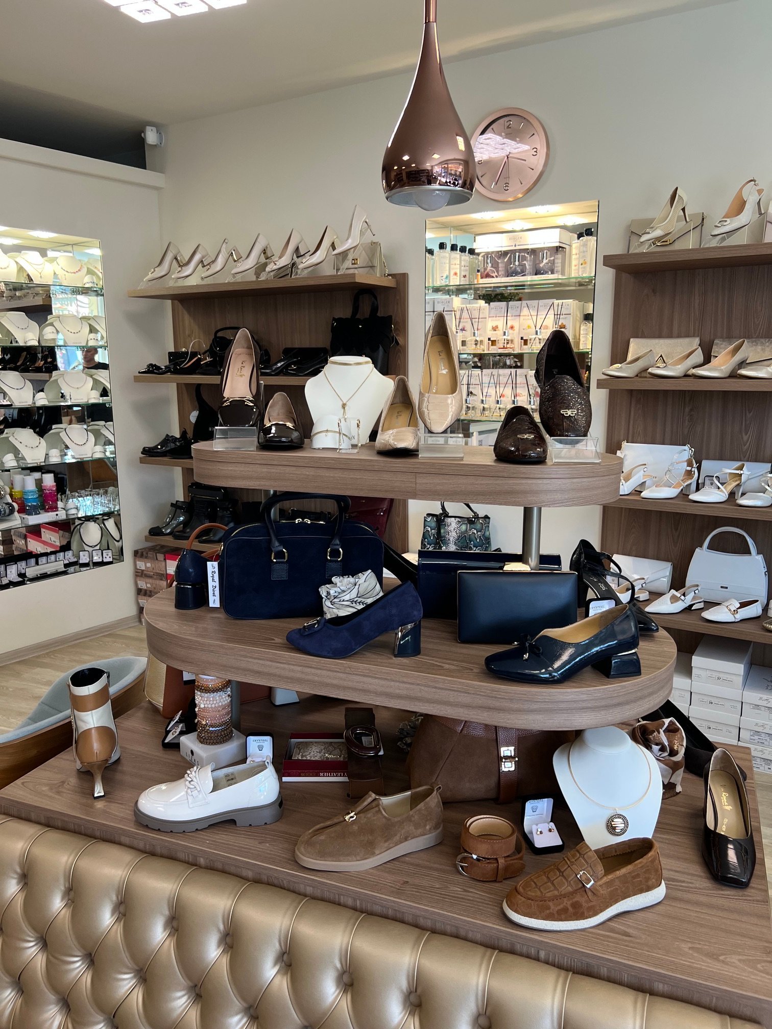 Upscale retail shoe and accessories store interior with wooden curved display shelves, hanging pendant light, mannequins, and various shoes and bags arranged on multiple levels