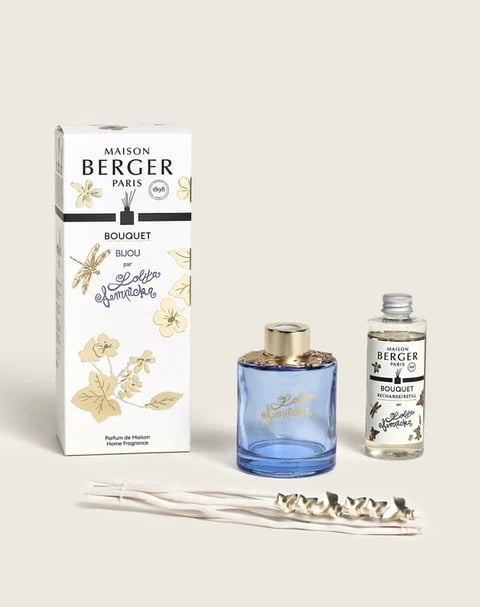 Maison Berger Paris fragrance bouquet set with blue glass diffuser bottle, white decorative reeds, and refill bottle on beige background