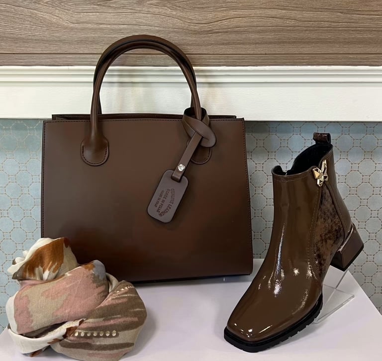 Brown leather tote bag with matching patent leather boots and accessories displayed on white surface