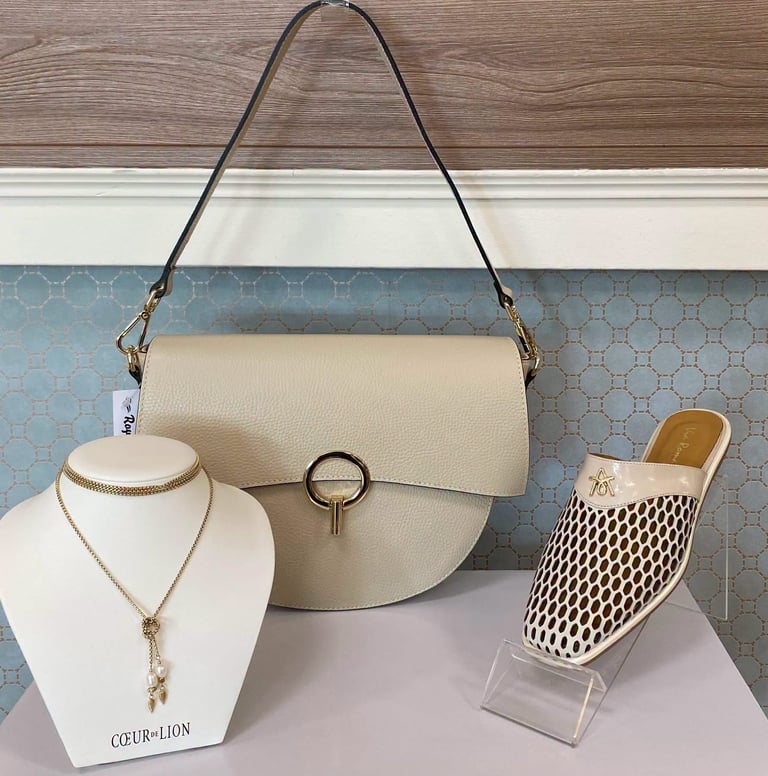 Beige handbag displayed with gold necklace on mannequin and white mesh shoe on stand in retail window