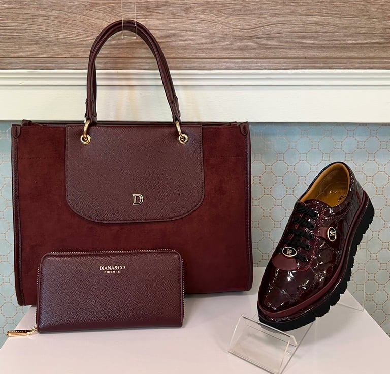 Burgundy leather tote bag, matching wallet, and black patent loafer shoe displayed on white surface