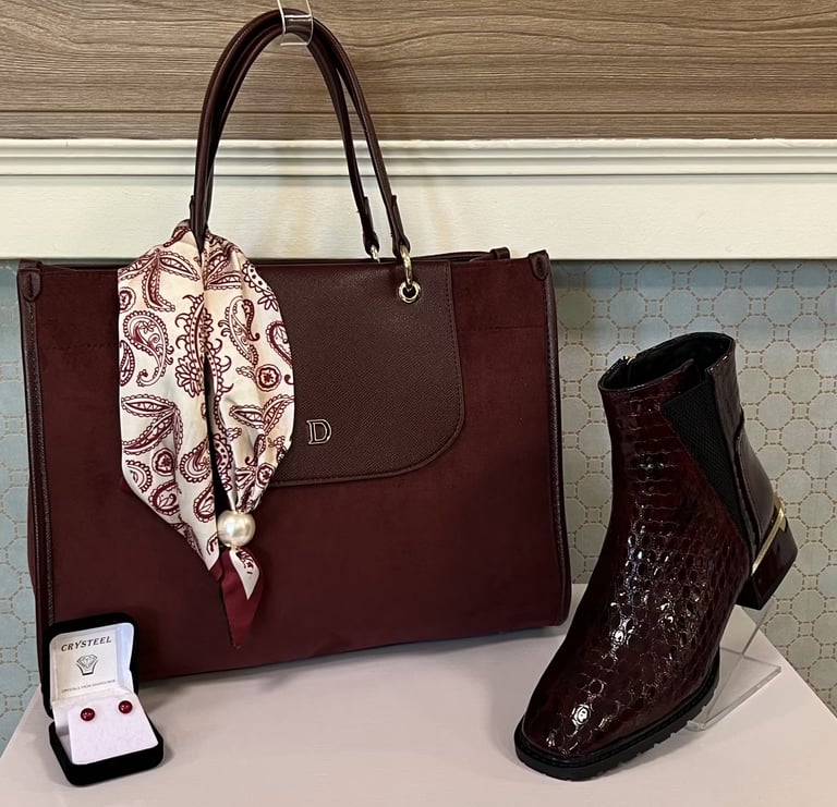 Burgundy leather tote bag with decorative scarf, paired with burgundy sequined boots and jewelry display on white surface