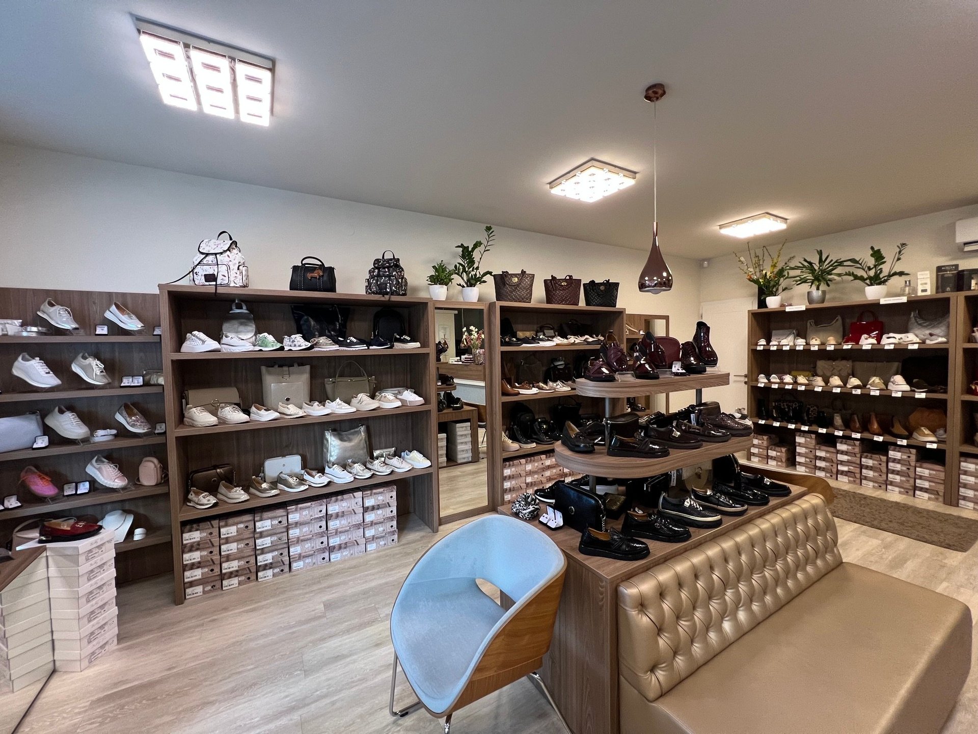 Modern shoe store interior with wooden shelving displaying sneakers, boots, and accessories, featuring a blue accent chair and organized product display
