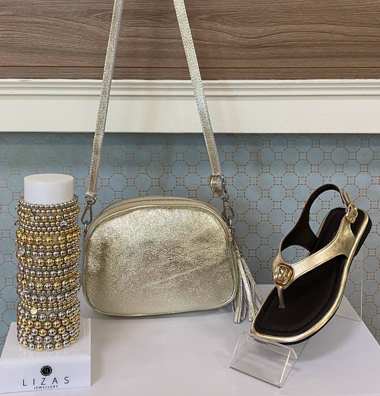 Three gold-toned accessories displayed on a pedestal: a beaded clutch, a crossbody shoulder bag, and a slingback sandal